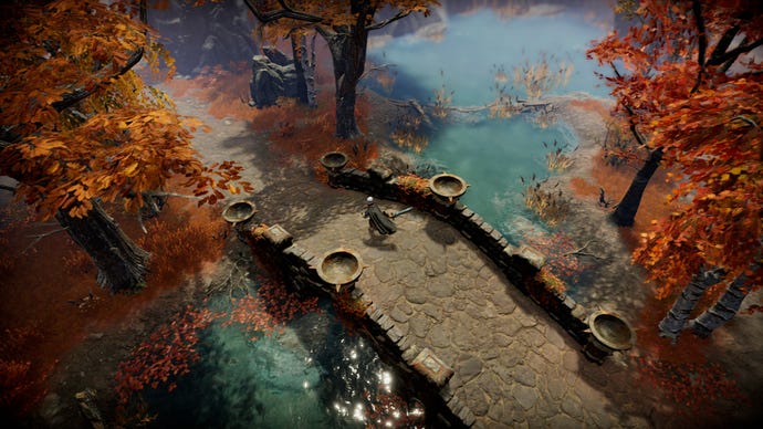 A player in V Rising crosses a bridge over a river surrounded by auburn-coloured trees.