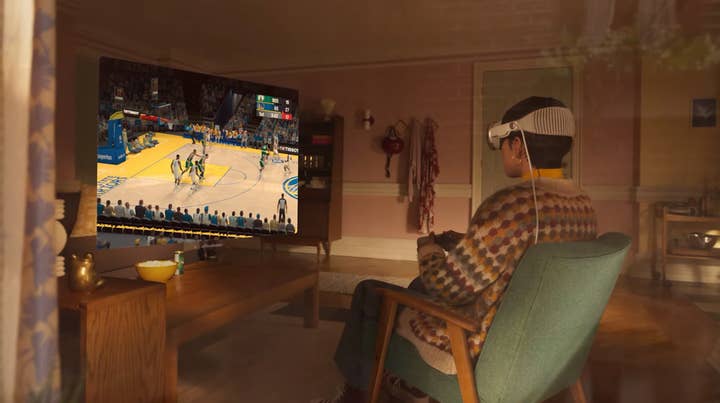 A woman sits in a chair wearing Apple's Vision Pro headset. In front of her, a virtual screen showing NBA 2K23 floats above a coffee table