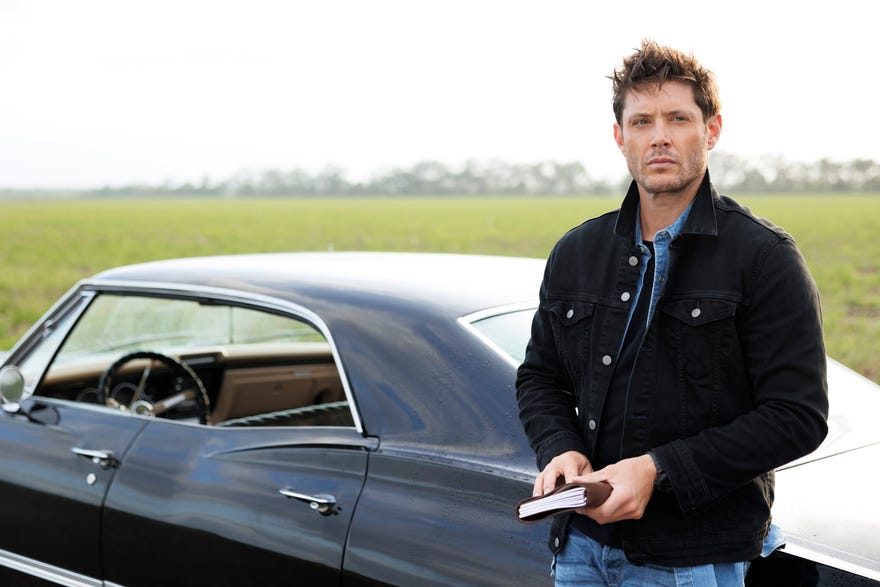Jensen Ackles as Dean WInchester, holding a notebook leaning against a car
