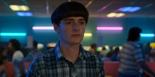 Will Byers in skating rink with bright lights behind him