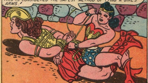 A panel from Sensation Comics #35 by William Moulton Marston and Harry G. Peter. Wonder Woman has pinned another woman in armor face down on the ground and is sitting on the other woman's thighs, facing her feet. The other woman's knees are bent, and Wonder Woman's legs are locked around the other woman's calves. Wonder Woman is twisting around to tie the other woman's wrists behind her back and saying, "On Paradise Island where we play many binding games this is considered the safest method of tying a girl's arms!"