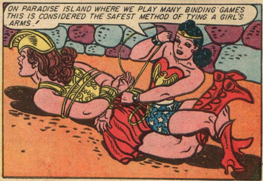 A panel from Sensation Comics #35 by William Moulton Marston and Harry G. Peter. Wonder Woman has pinned another woman in armor face down on the ground and is sitting on the other woman's thighs, facing her feet. The other woman's knees are bent, and Wonder Woman's legs are locked around the other woman's calves. Wonder Woman is twisting around to tie the other woman's wrists behind her back and saying, "On Paradise Island where we play many binding games this is considered the safest method of tying a girl's arms!"