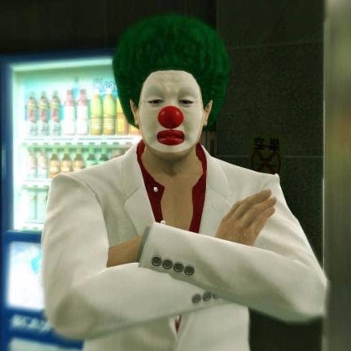 A character from Yakuza Kiwami wearing a white suit with red open-collared shirt, standing with his arms crossed. He has a bushy green wig, red bulbous clown nose, and his face is painted white